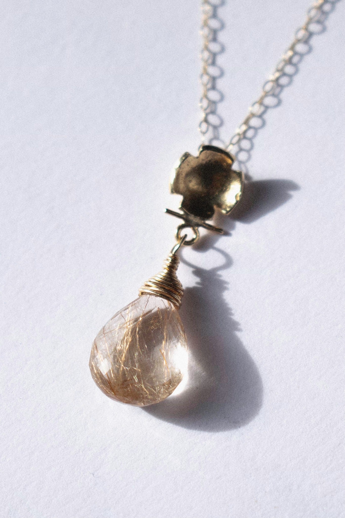a gold pendant with rutilated quartz on a white background