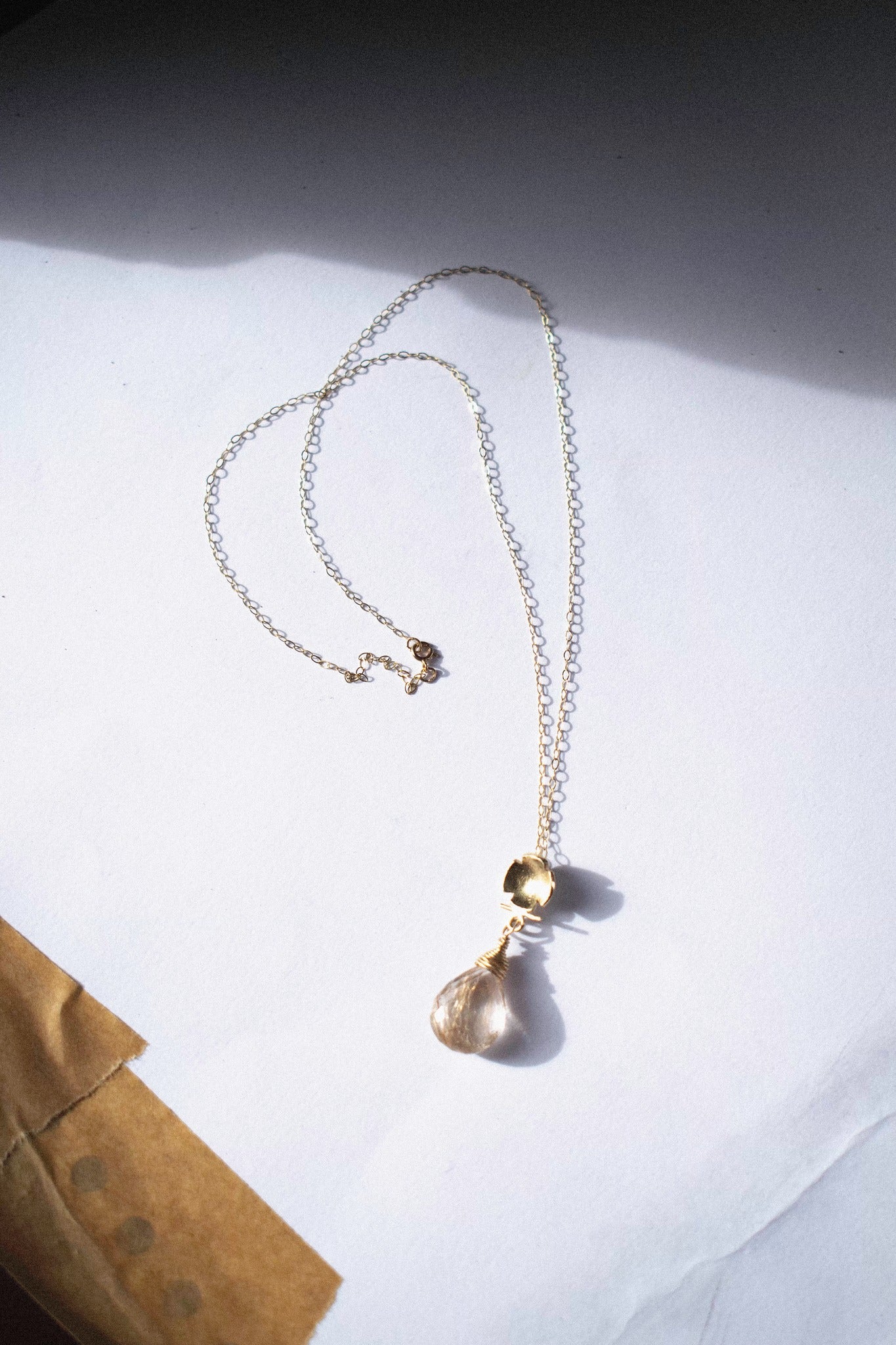 a gold pendant with rutilated quartz on a white background