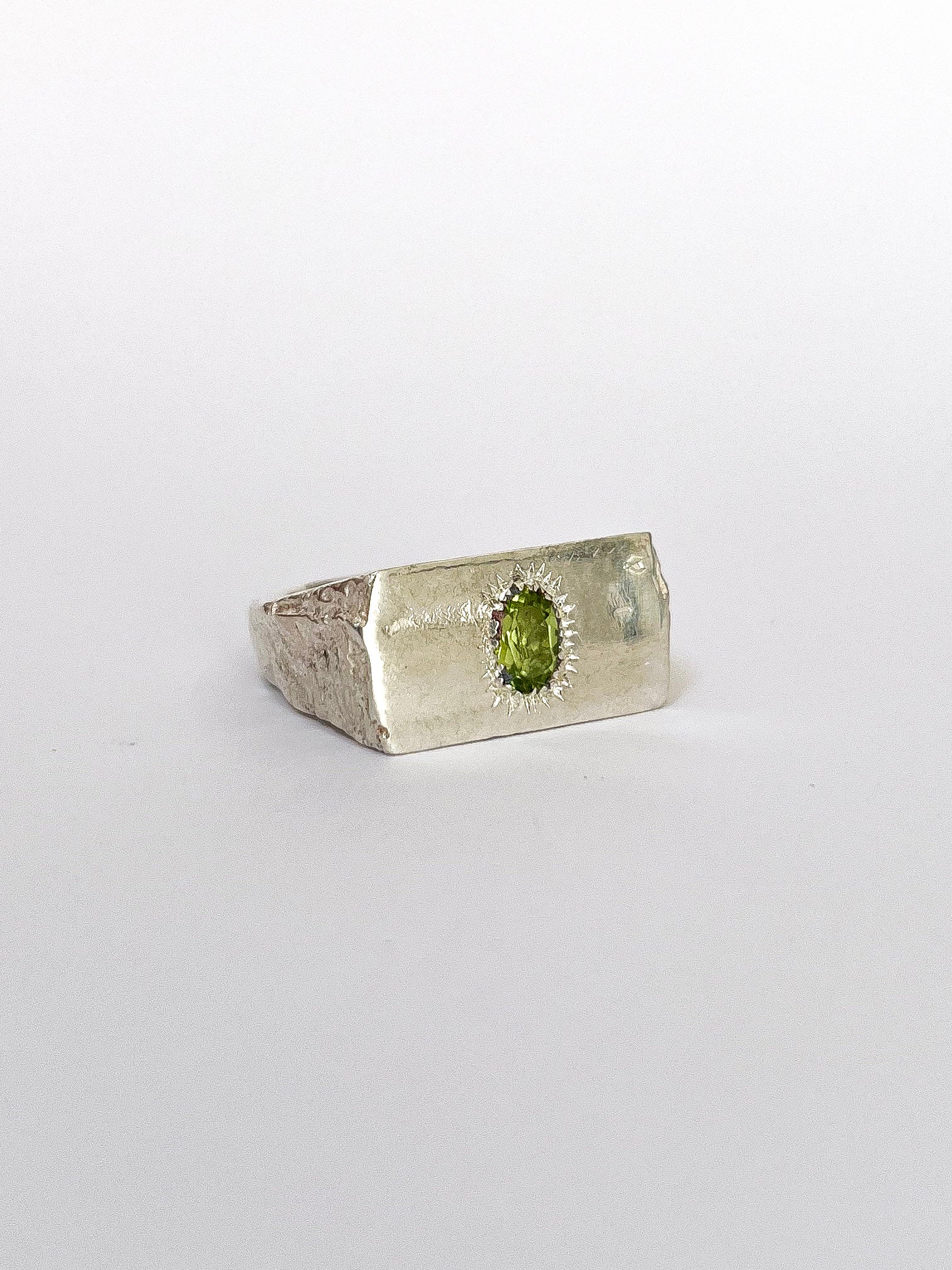 a silver signet ring with peridot on a white background