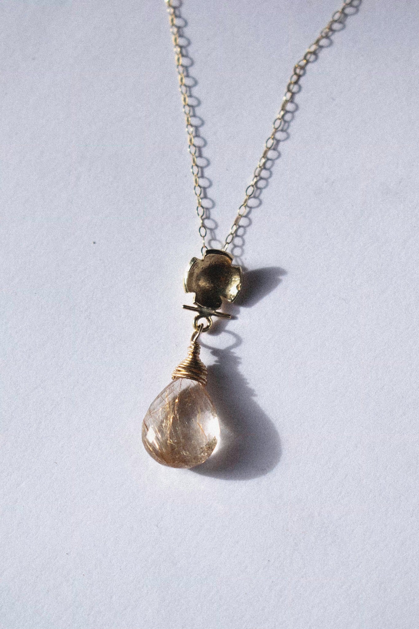a gold pendant with rutilated quartz on a white background