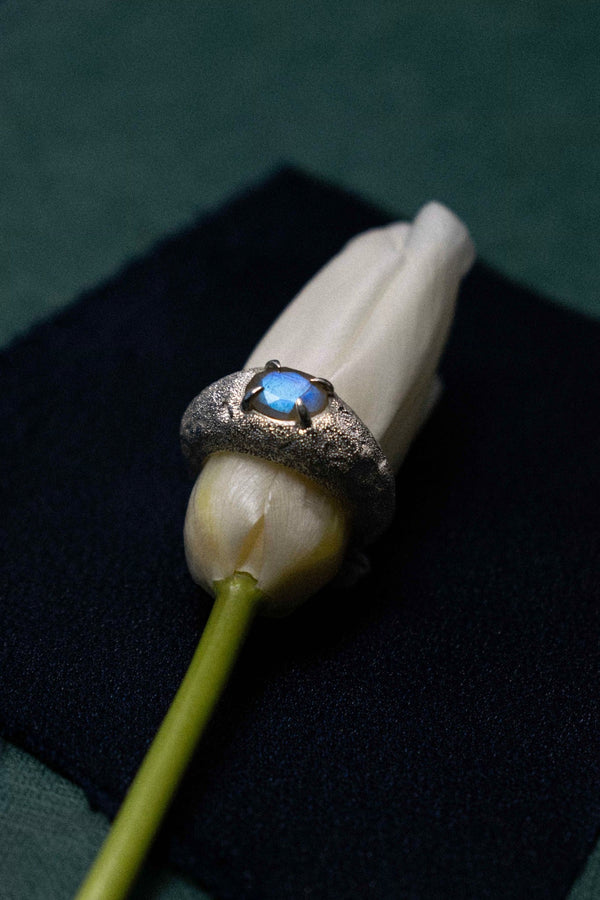 a handmade silver and labradorite ring on a white tulip against a dark and green background