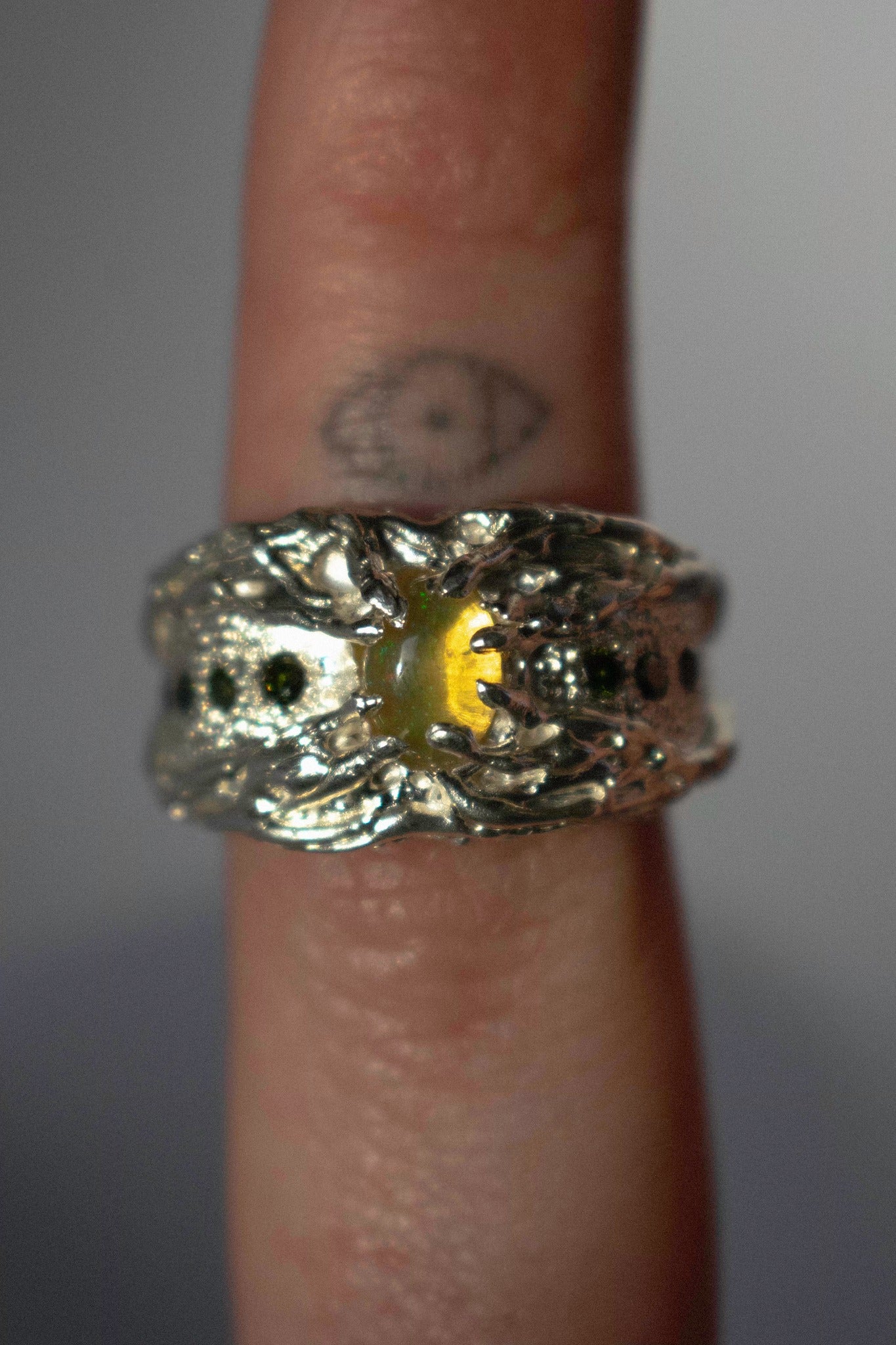 a large silver ring with opal and green diamonds on a hand