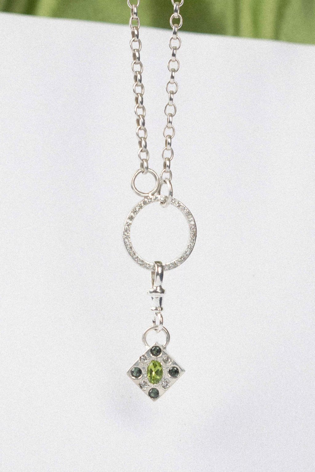 a diamond shaped charm with green gemstone in silver on a white background