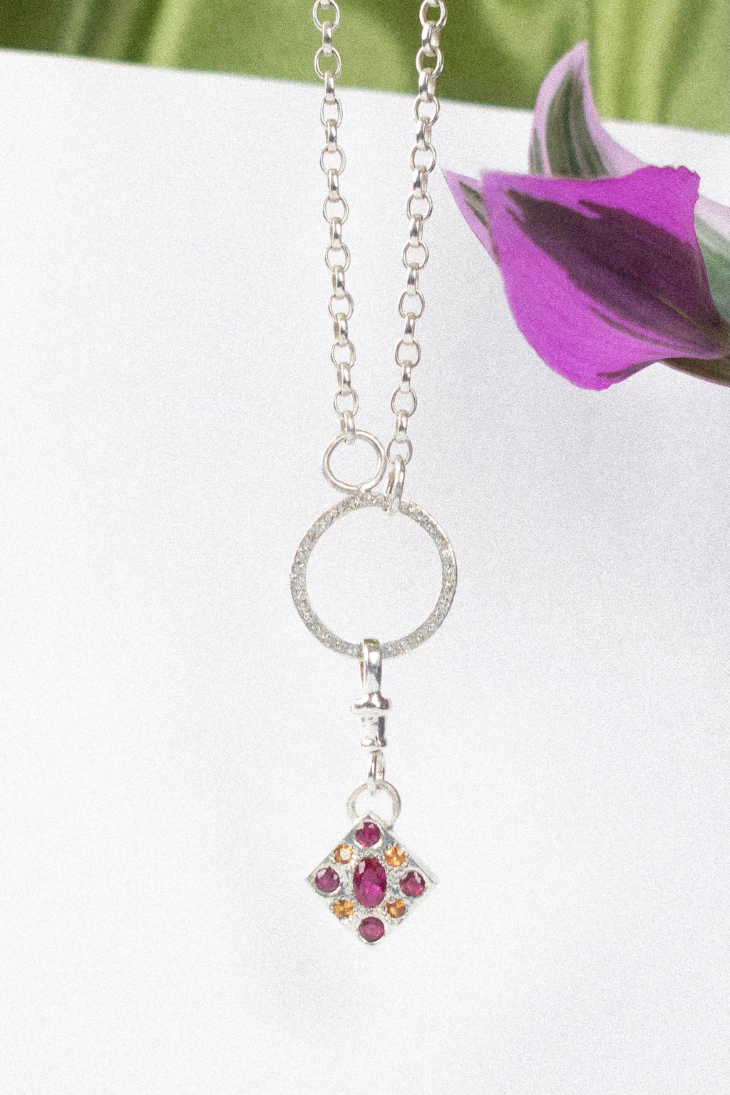 a diamond shaped charm with pink gemstone in silver on a white background