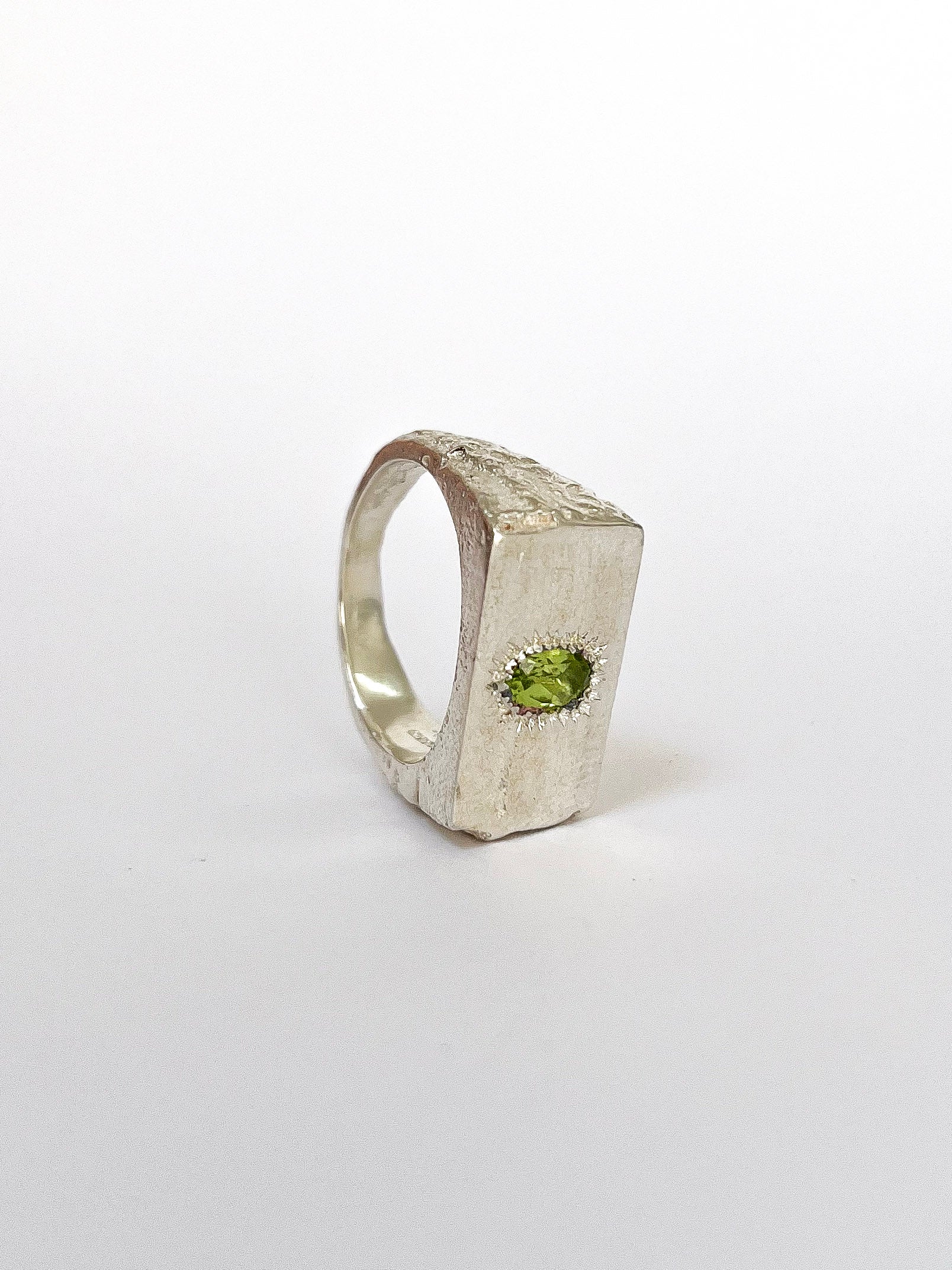 a silver signet ring with peridot on a white background 