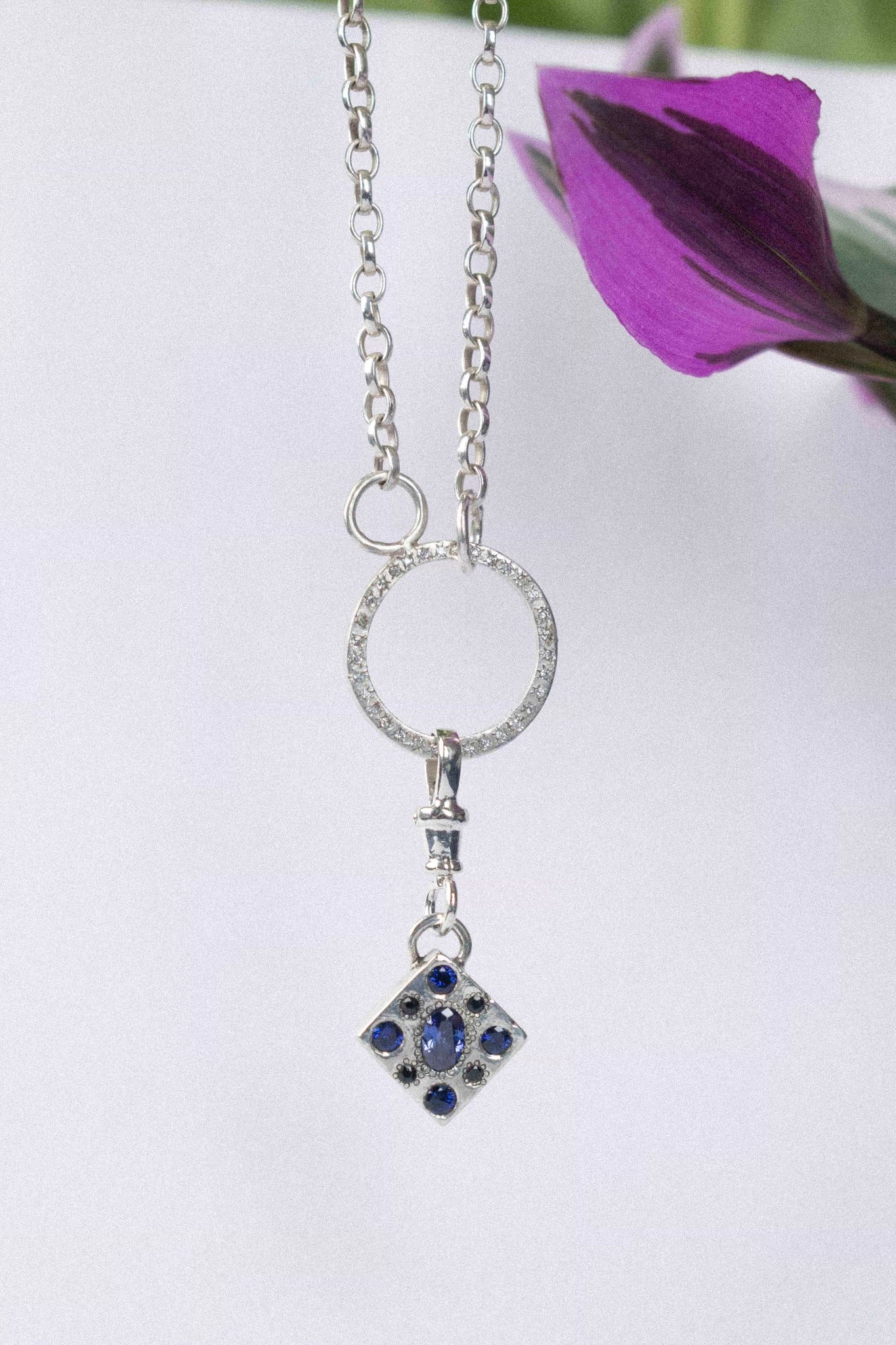 a diamond shaped charm with blue gemstone in silver on a white background