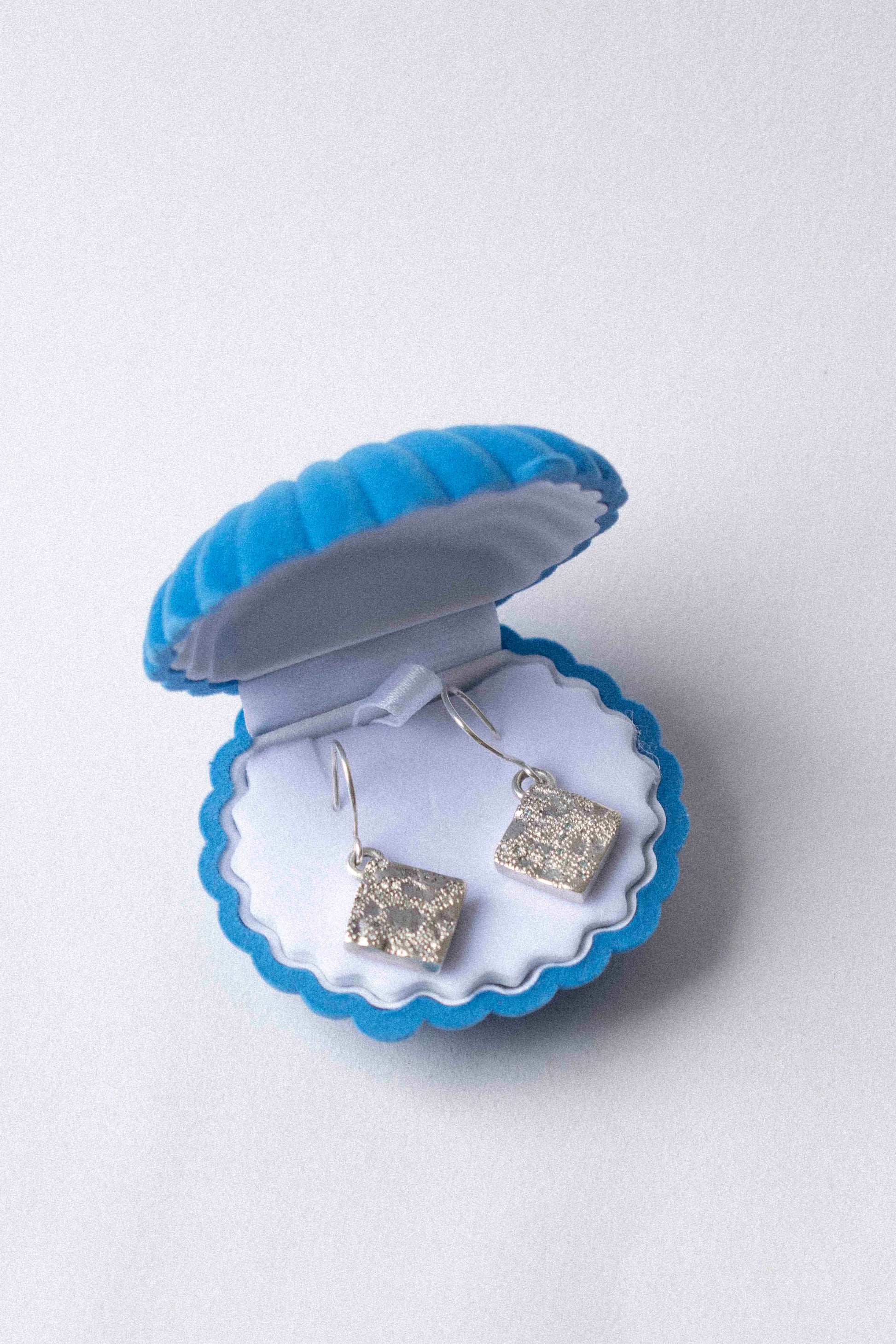 two diamond shaped silver earring displayed in a shell shaped jewellery box