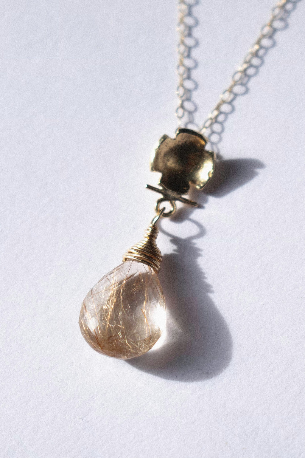 a gold pendant with rutilated quartz on a white background 