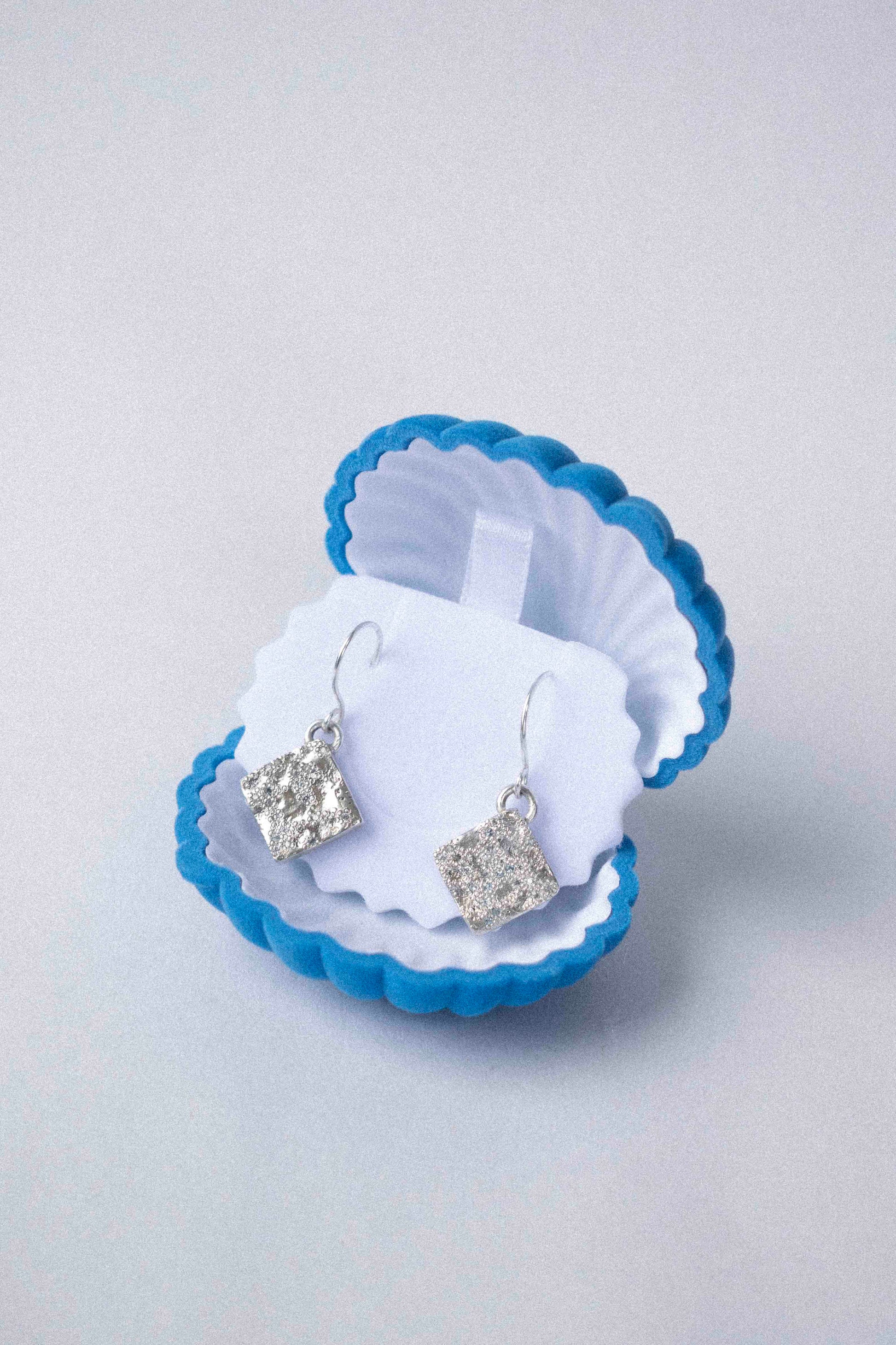 two diamond shaped silver earring displayed in a shell shaped jewellery box