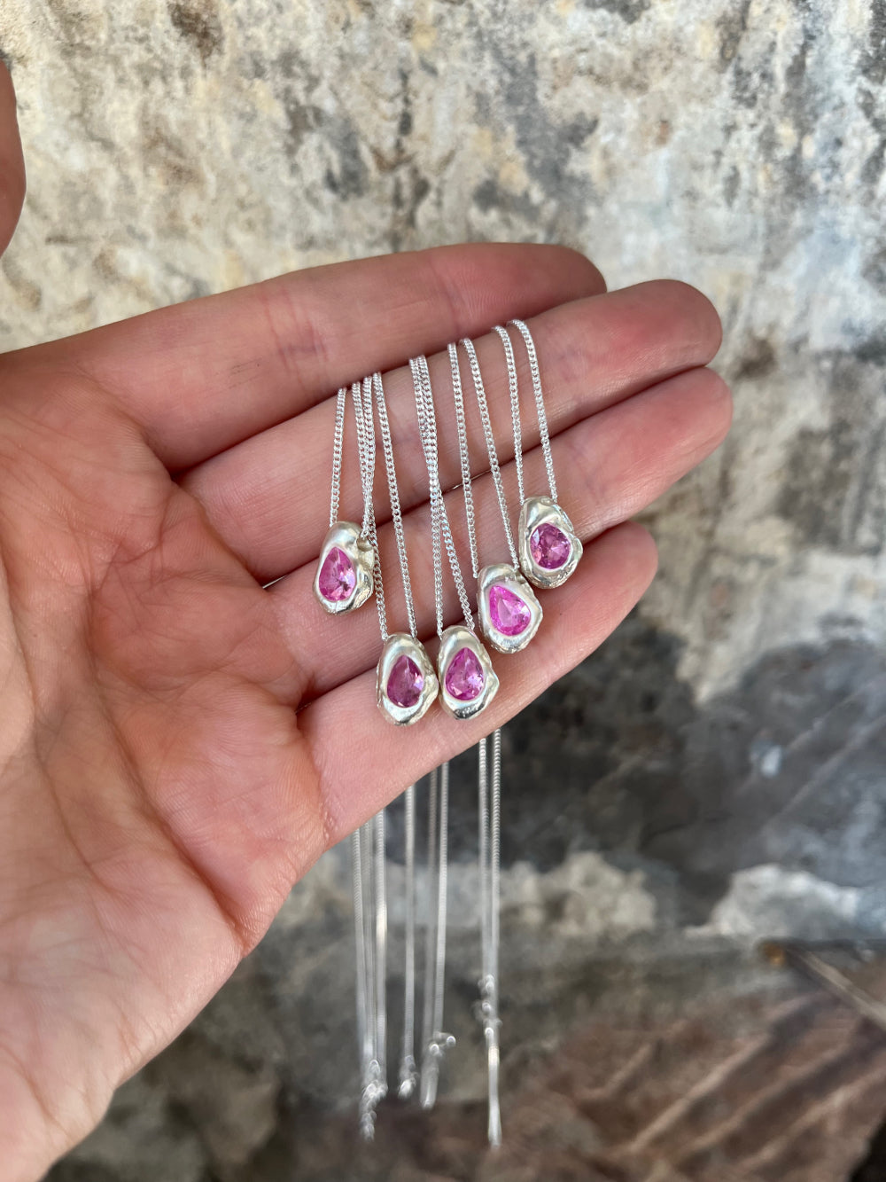 five small silver pendants pink cast in place stones held by a hand