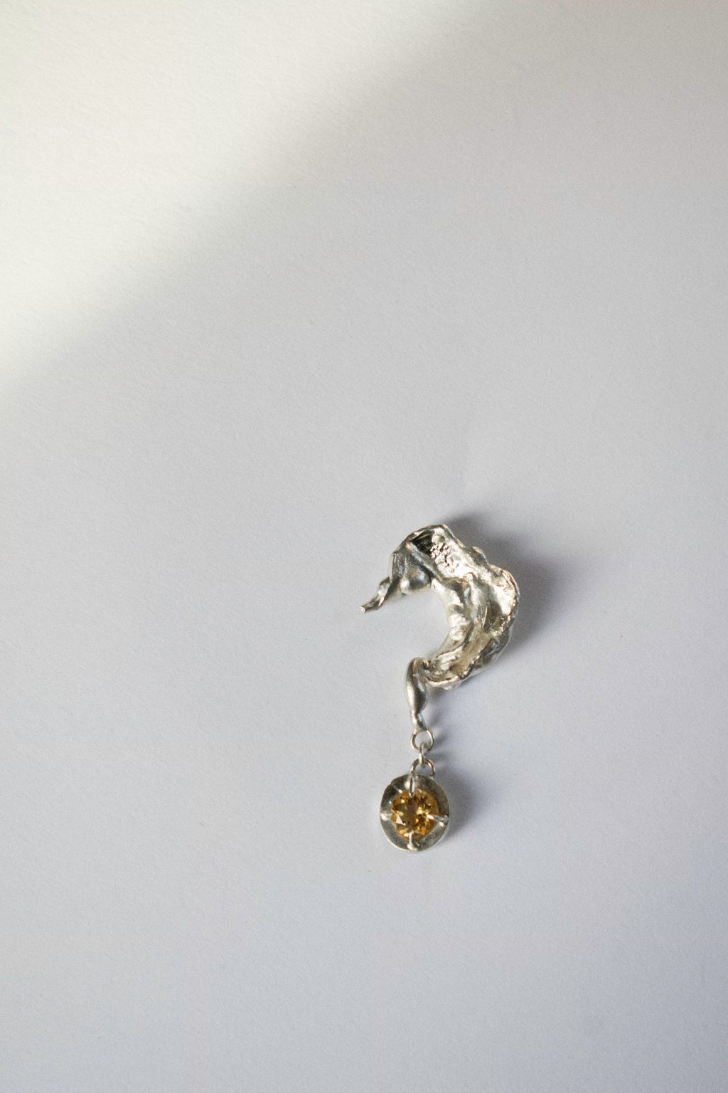 silver earring in the shape of a question mark on a white background