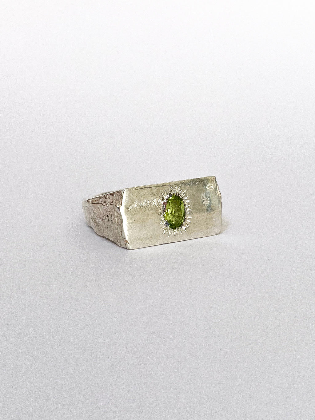 a silver signet ring with peridot on a white background 