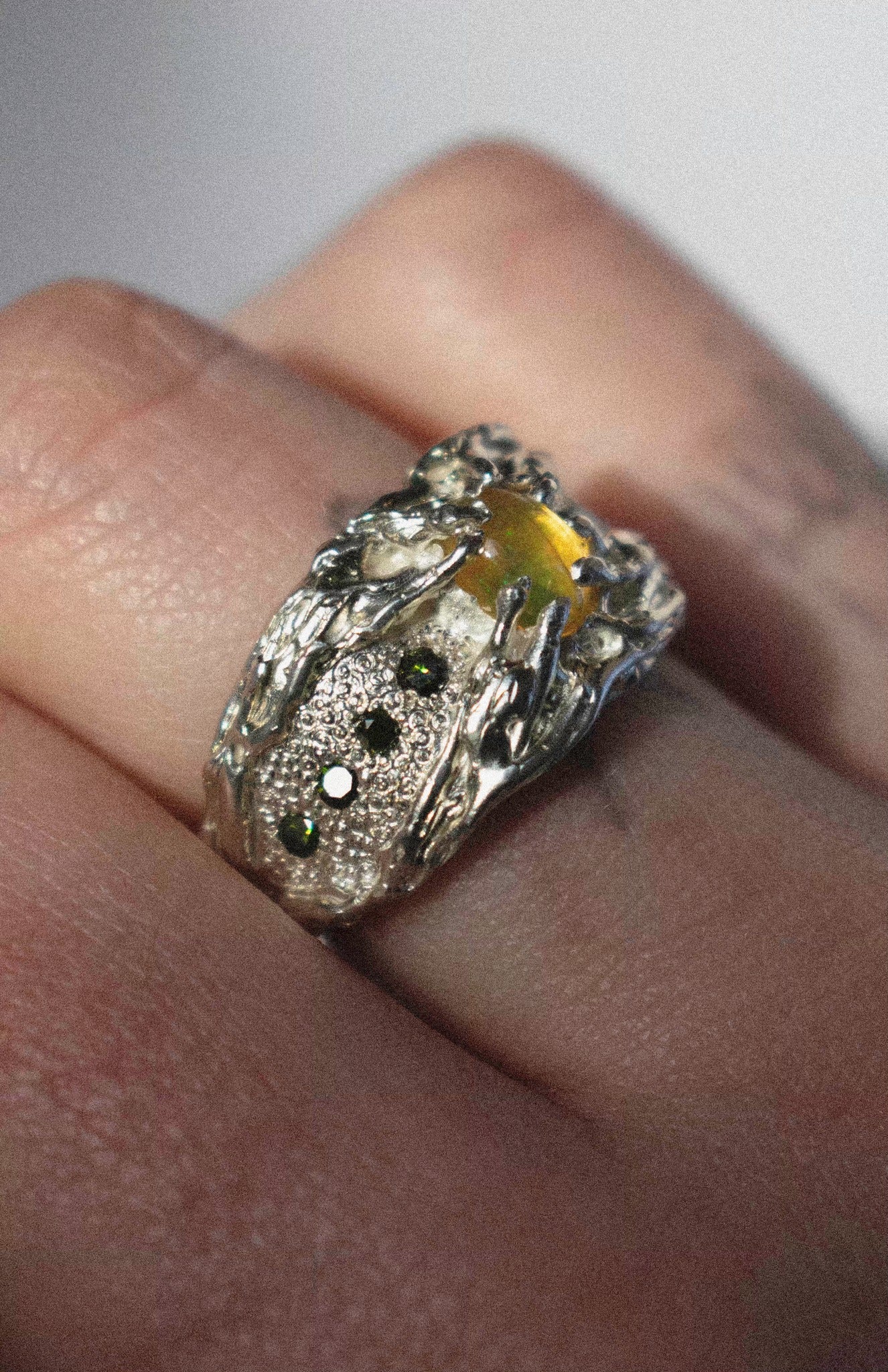 a large silver ring with opal and green diamonds on a hand