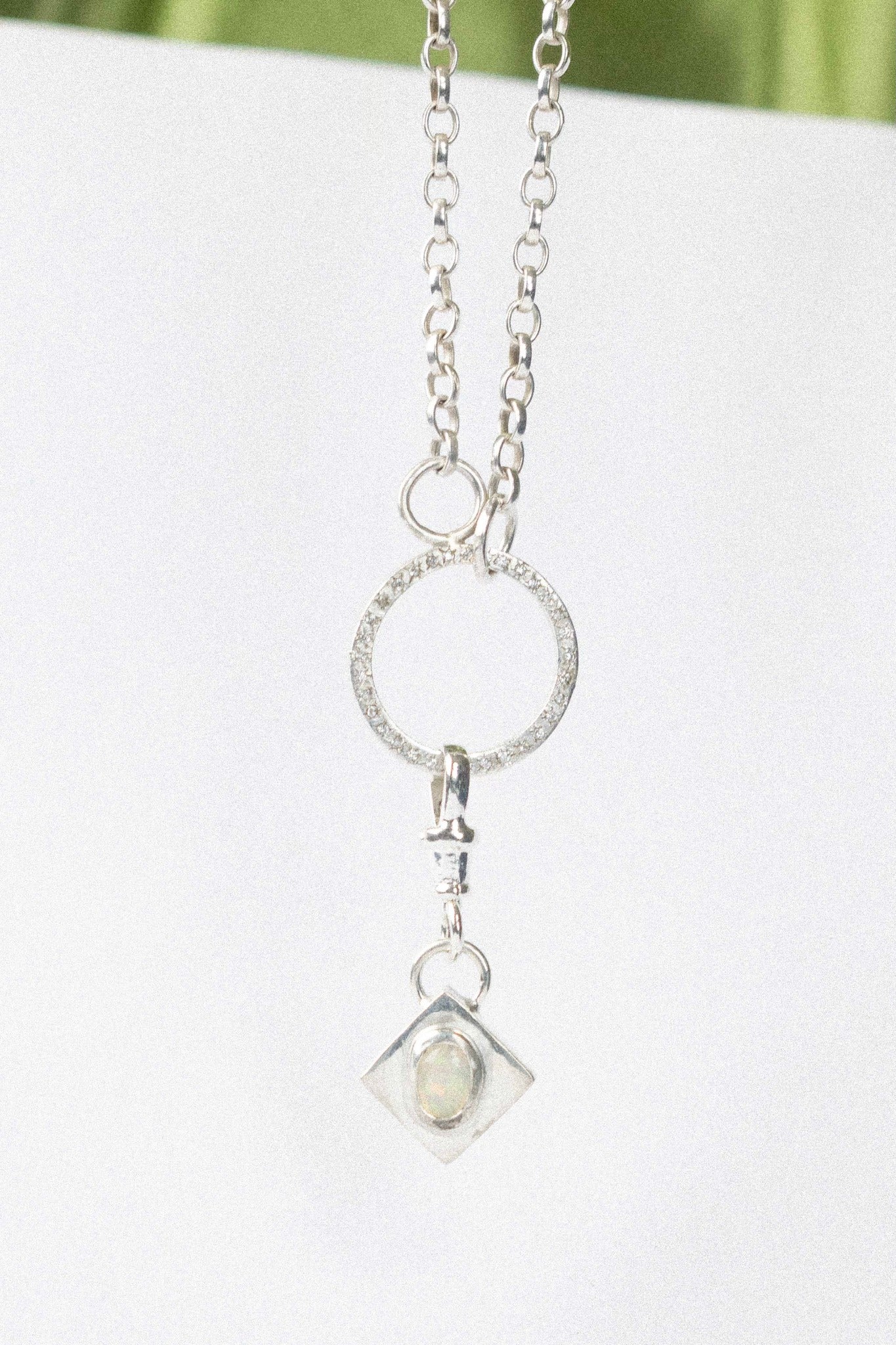 opal charm hanging on a silver necklace on a white background