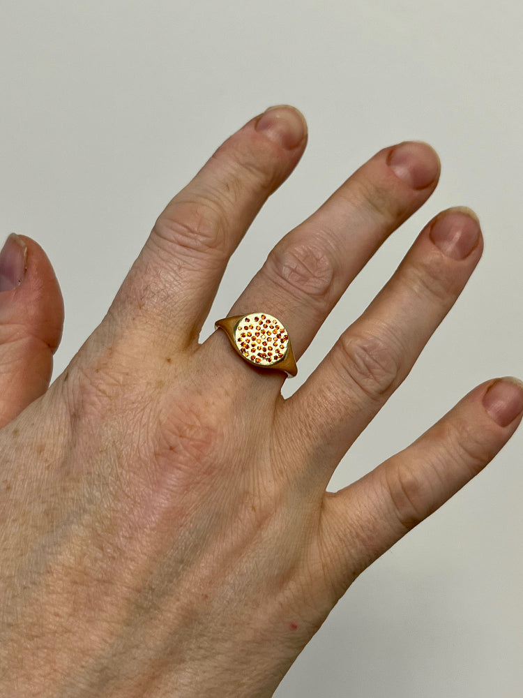 gold signet ring with orange gemstones on a woman's hand
