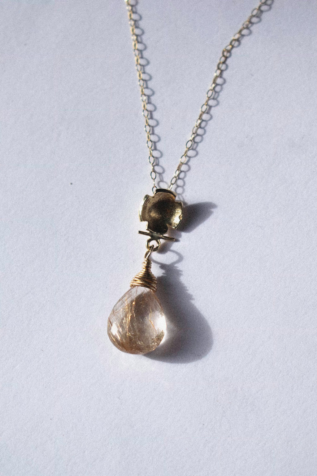 a gold pendant with rutilated quartz on a white background 