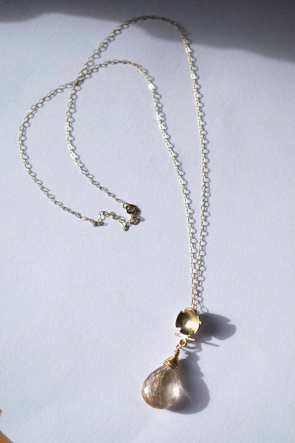 a gold pendant with rutilated quartz on a white background 