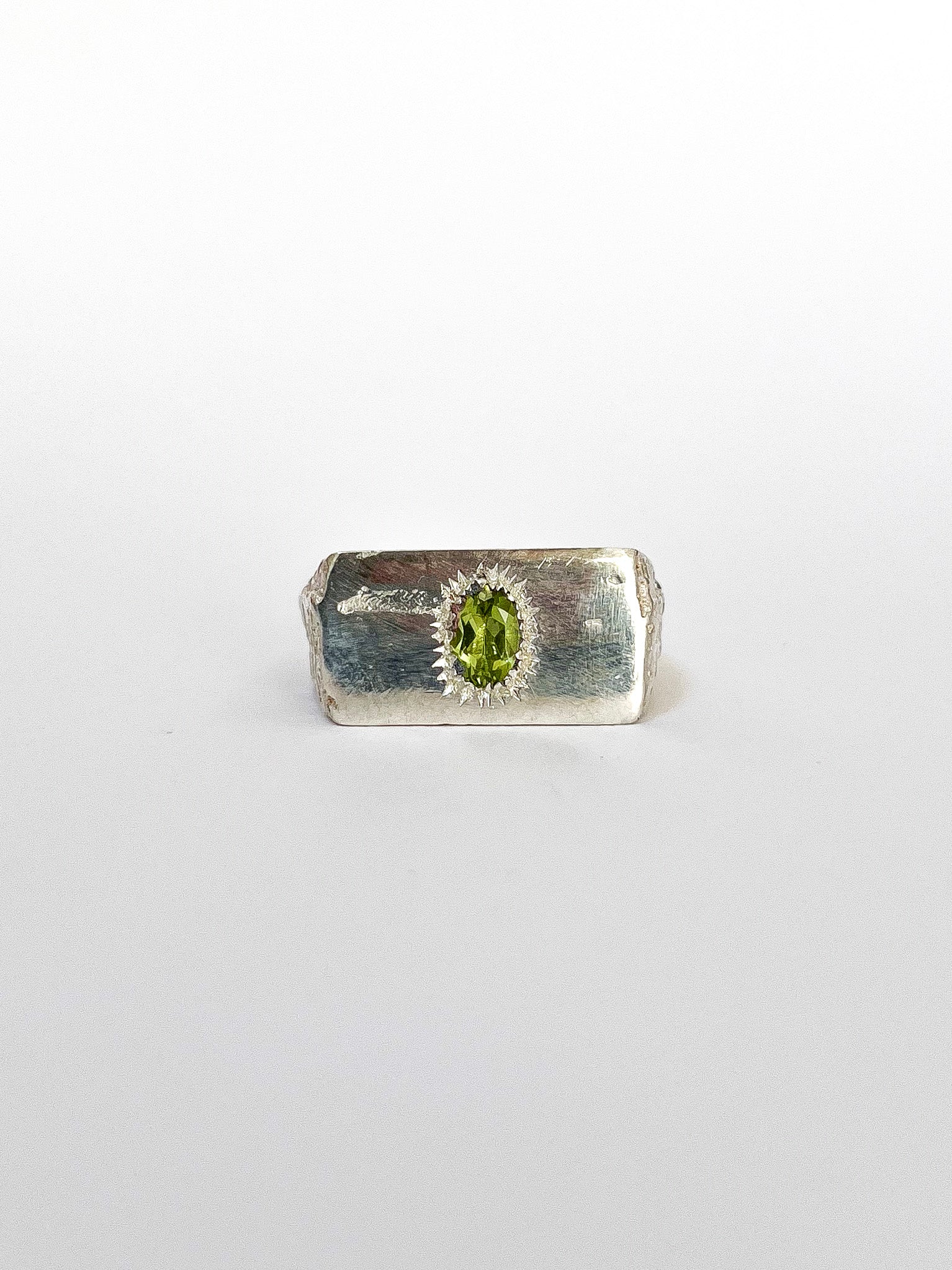 a silver signet ring with peridot on a white background 