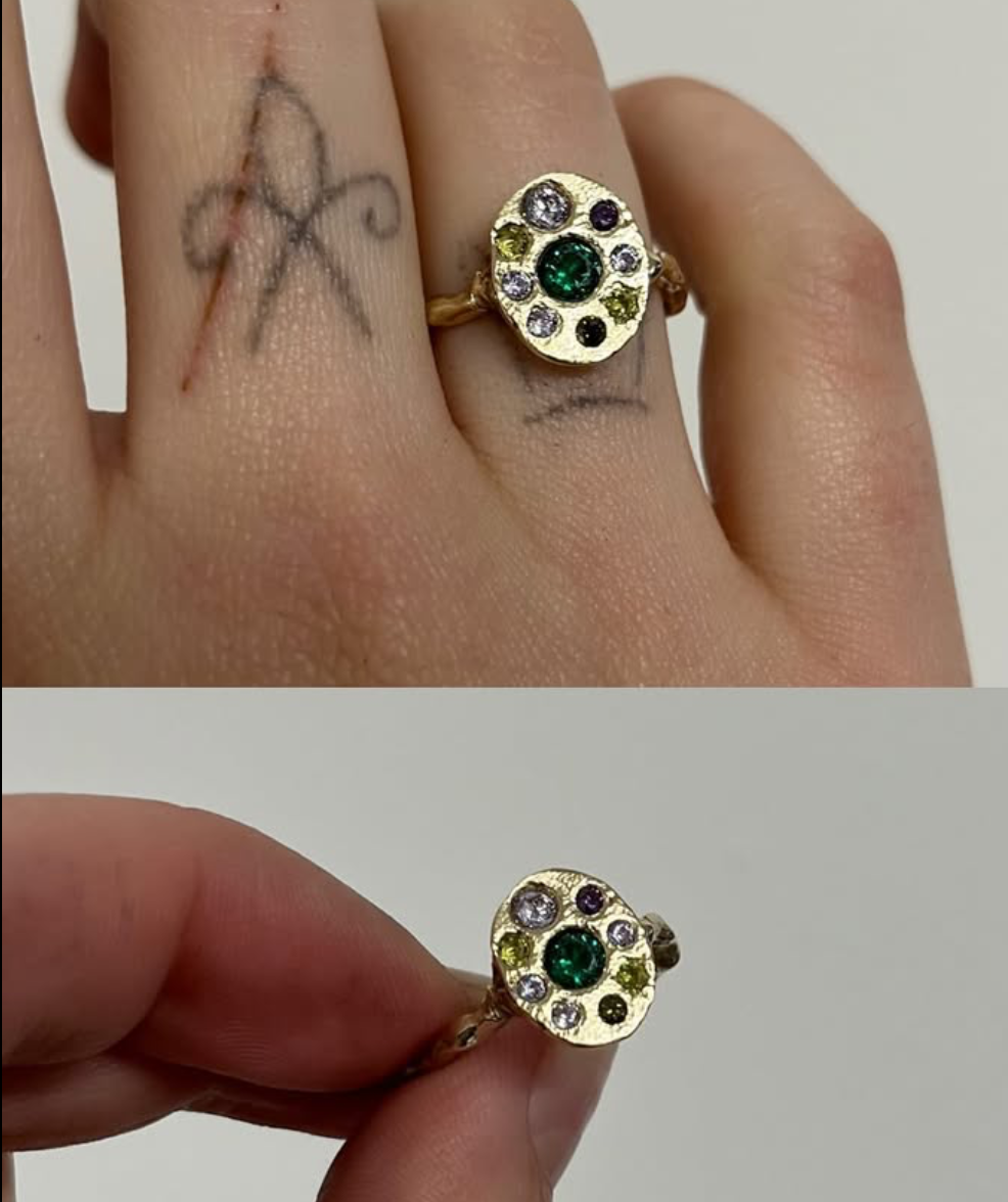 woman hand wearing a gold ring with purple and green gemstones