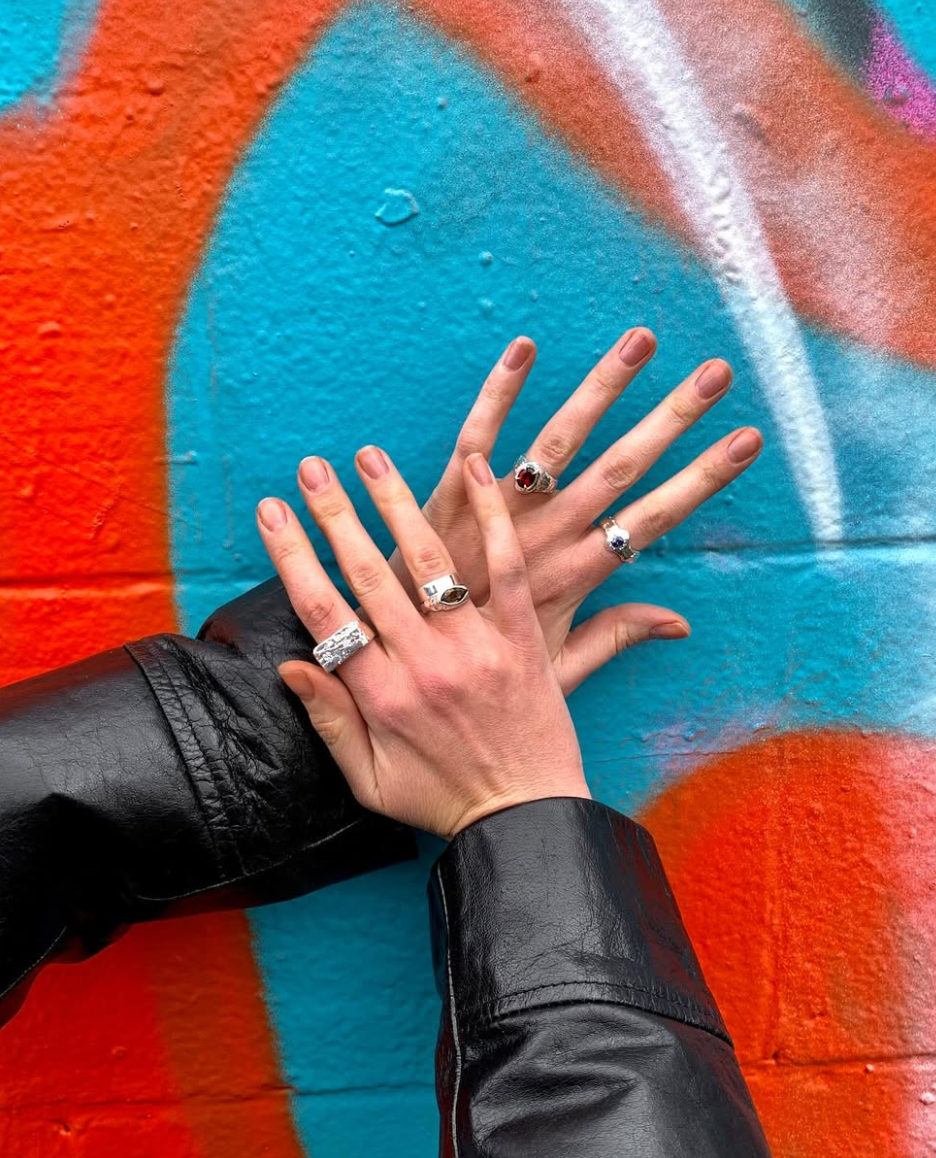 womans hands wearing handmade silver rings on a red and blue background