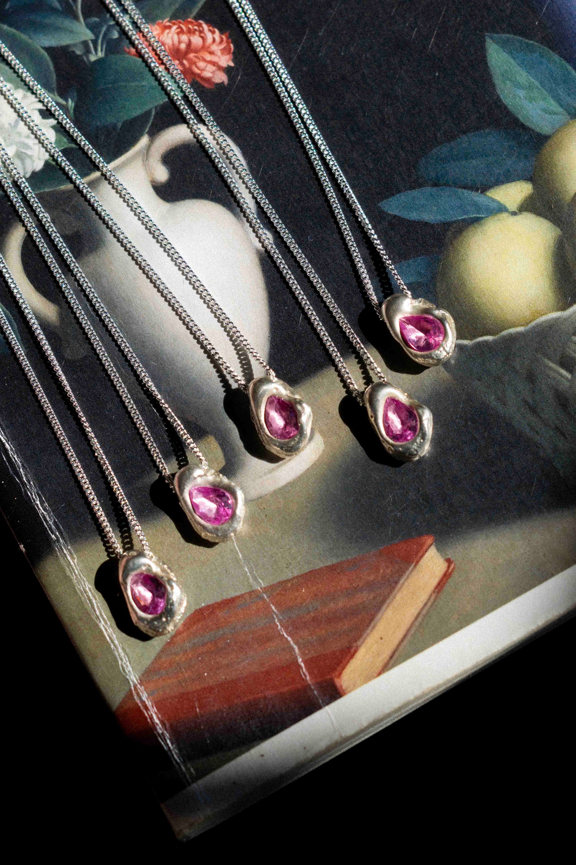 five small silver pendants laid over a painting with pink cast in place stones