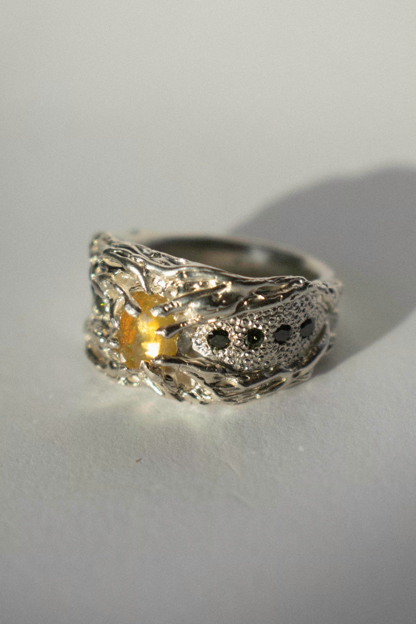 a large silver ring with opal and green diamonds on a white background