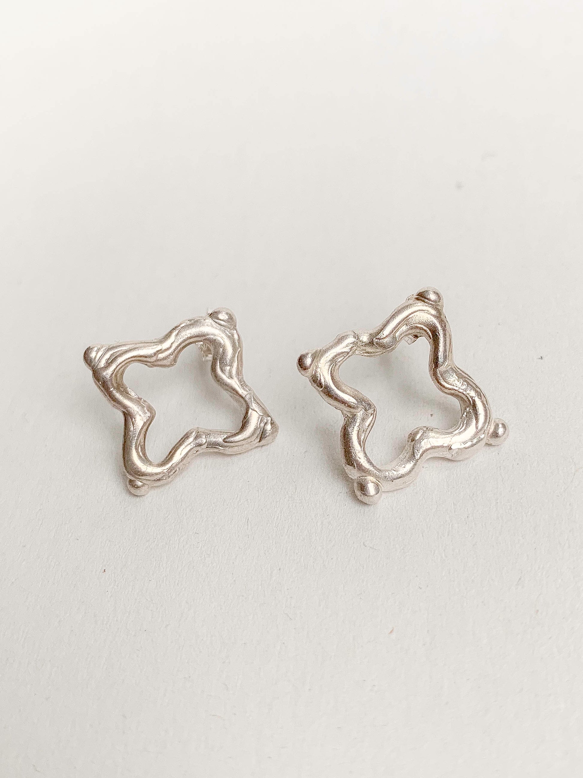 two silver earrings in the shape of quatrefoils on a white background