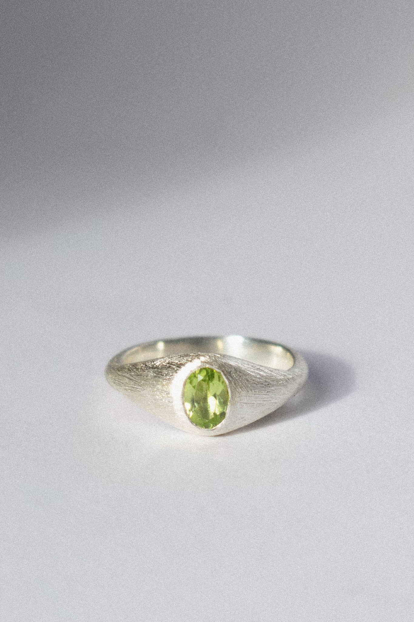 a silver bombé ring with a green peridot on a white background