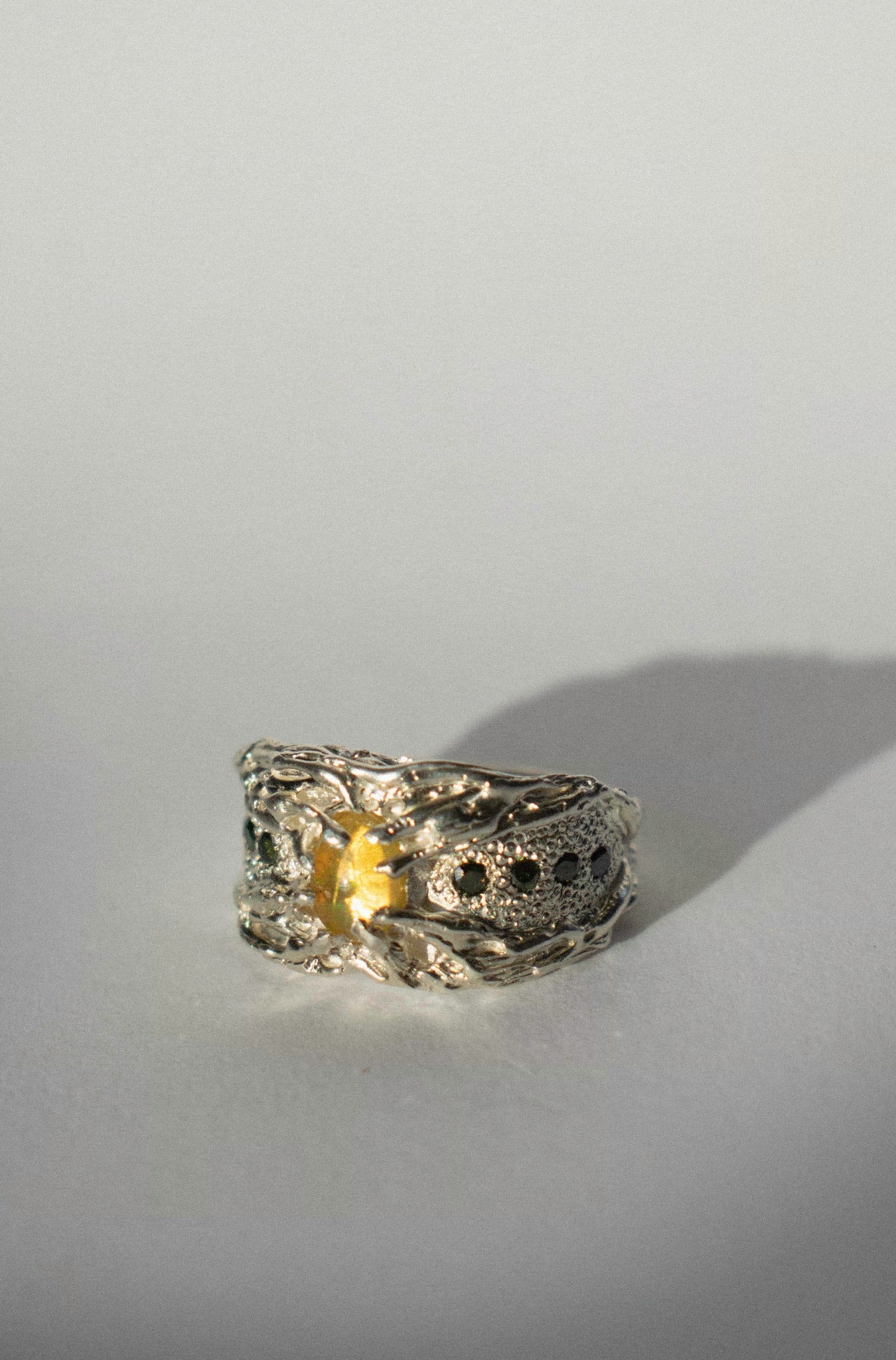 a large silver ring with opal and green diamonds on a white background