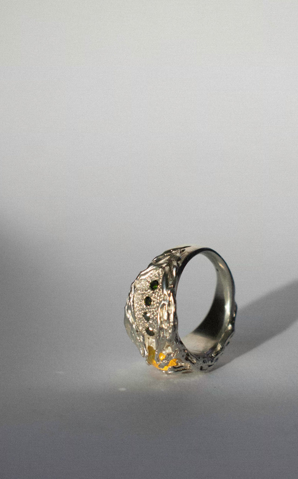 a large silver ring with opal and green diamonds on a white background