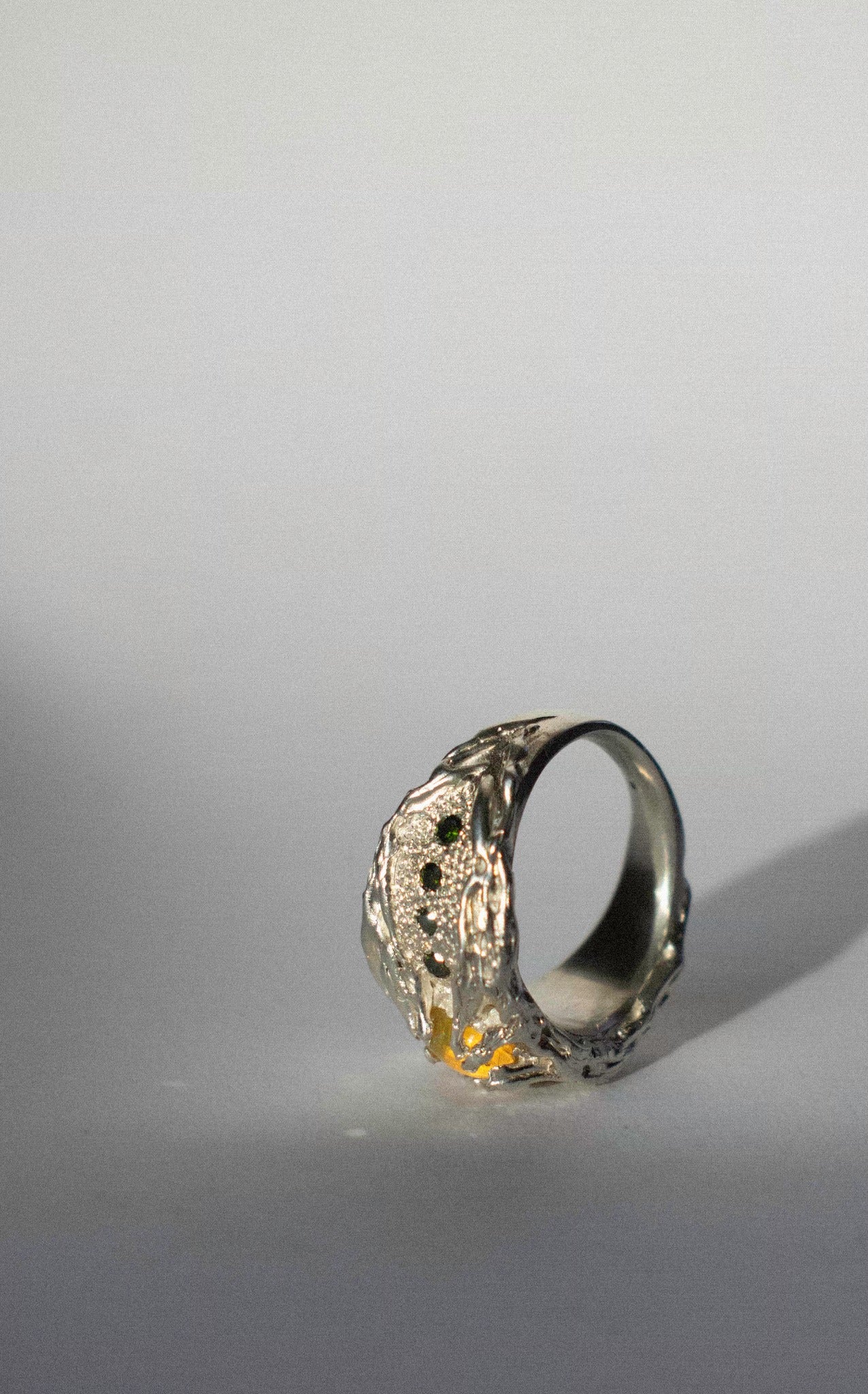 a large silver ring with opal and green diamonds on a white background